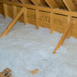 Unfinished attic with exposed wooden framing and a thick layer of white insulation on the floor.
